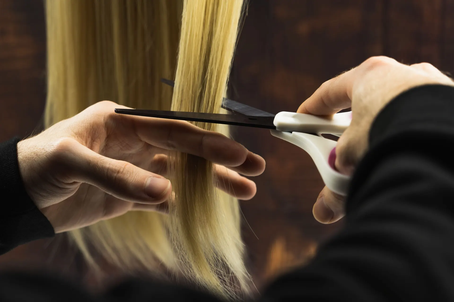 Kadeřnice stříhá konečky blond vlasů nůžkami